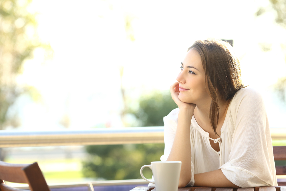 Pensive happy woman remembering looking at side sitting in a bar or home terrace