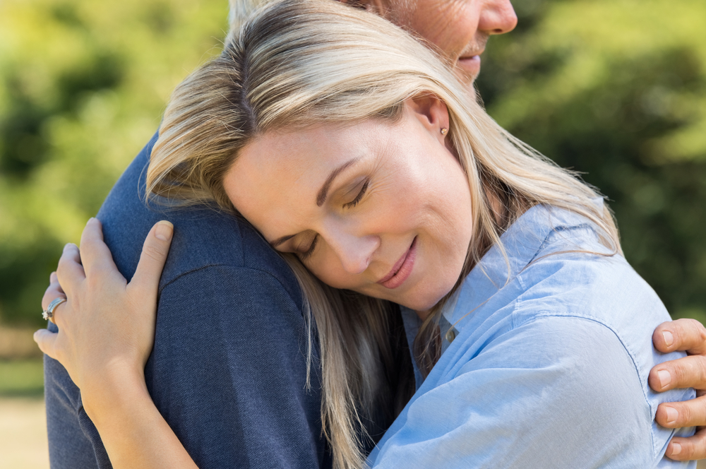 Close up face of senior woman with eyes closed hugging her husband. Romantic mature couple in love embracing outdoors. Satisfied senior wife hugging husband and feeling good.