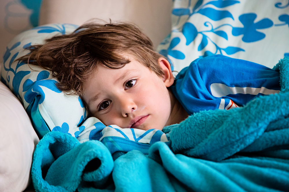 Sick child lying on couch at home having fever feeling ill. Getting well of flu. Kid with runny nose and sore throat