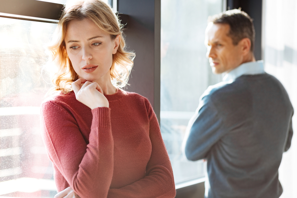 Problems in relationships. Sad unhappy cheerless woman standing near her boyfriend and holding her chin while feeling depressed