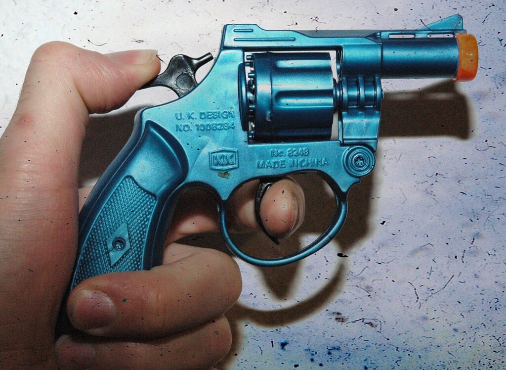An orange-tipped cap gun with its hammer drawn back

