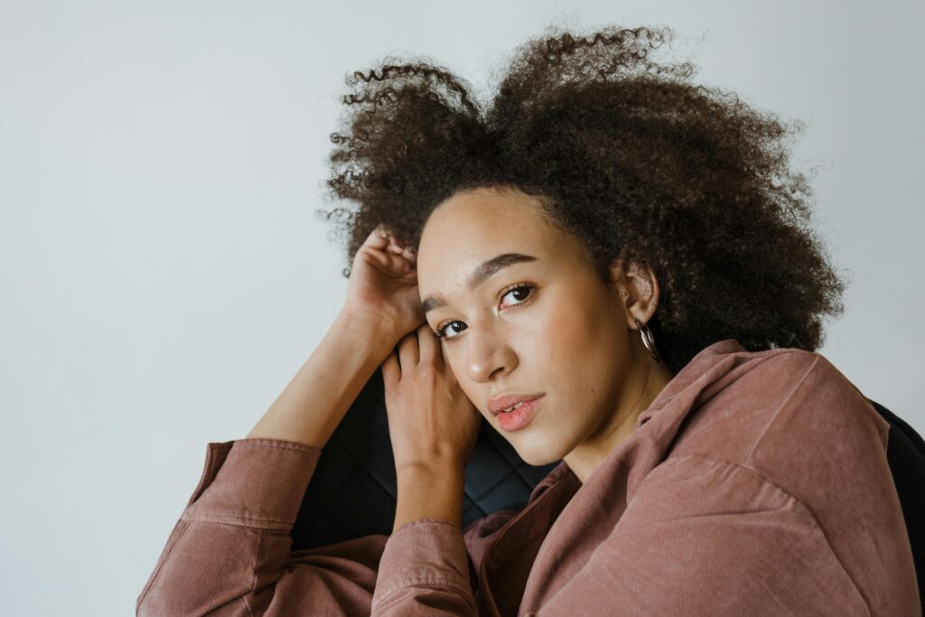 Thoughtful young black woman leaning on hand while resting in armchair