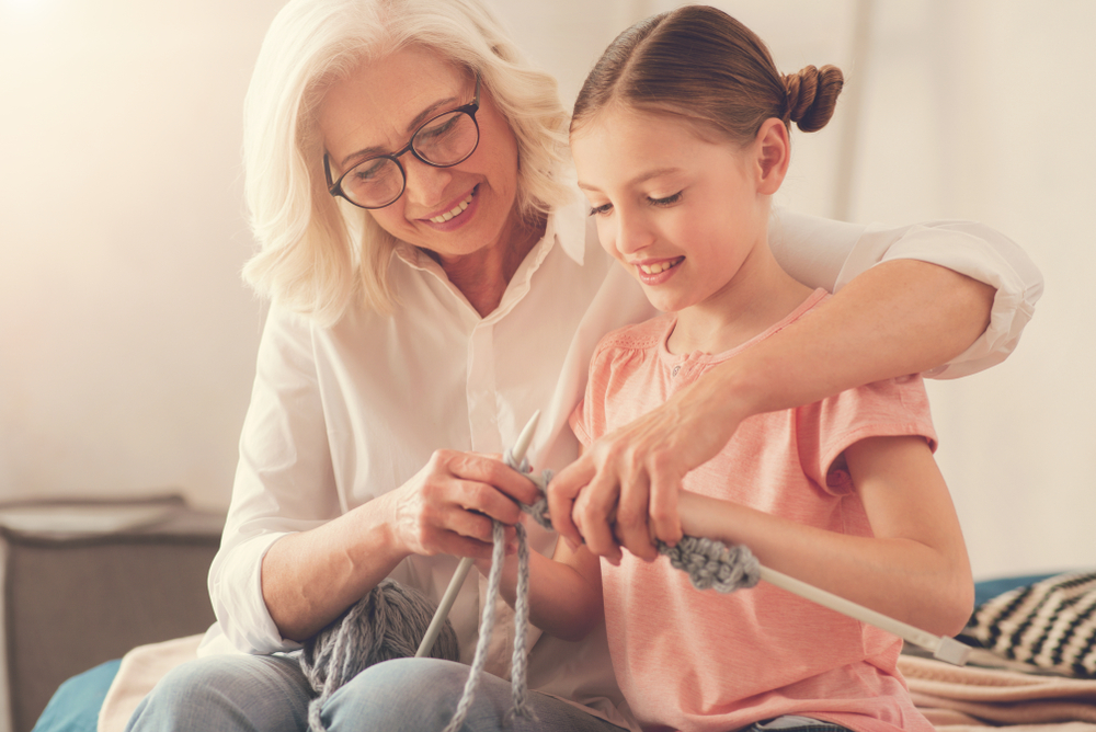 New skills. Nice pleasant elderly woman holding knitting needles and smiling while teaching her granddaughter to knit
