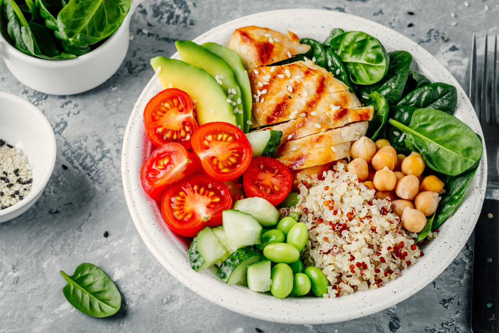 Buddha bowl with spinach salad, quinoa, roasted chickpeas, grilled chicken, avocado, tomatoes, cucumbers, sesame seeds.