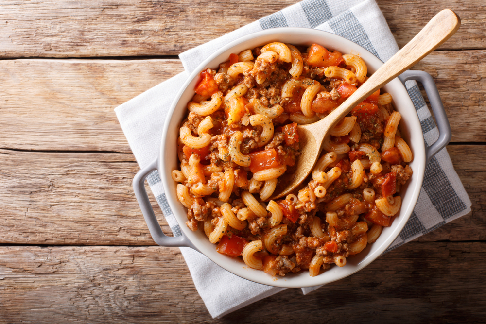 american chop suey, american goulash, with elbow pasta, beef and tomatoes close-up in a saucepan. horizontal top view from above
