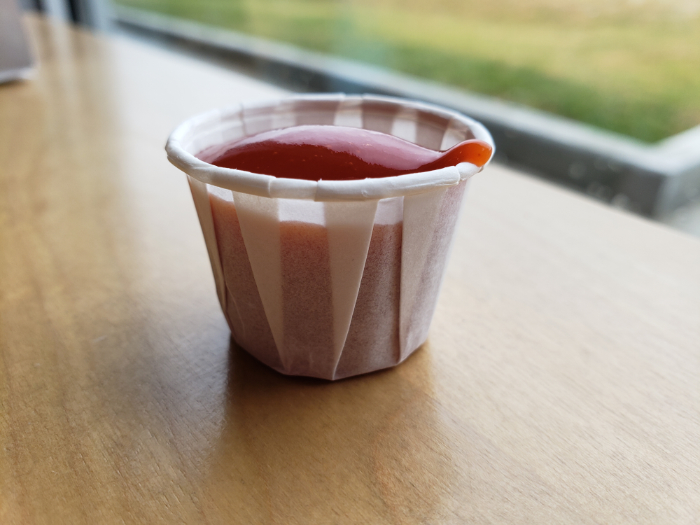 closeup of ketchup tomato sauce in a paper cup with blurred background under natural light

