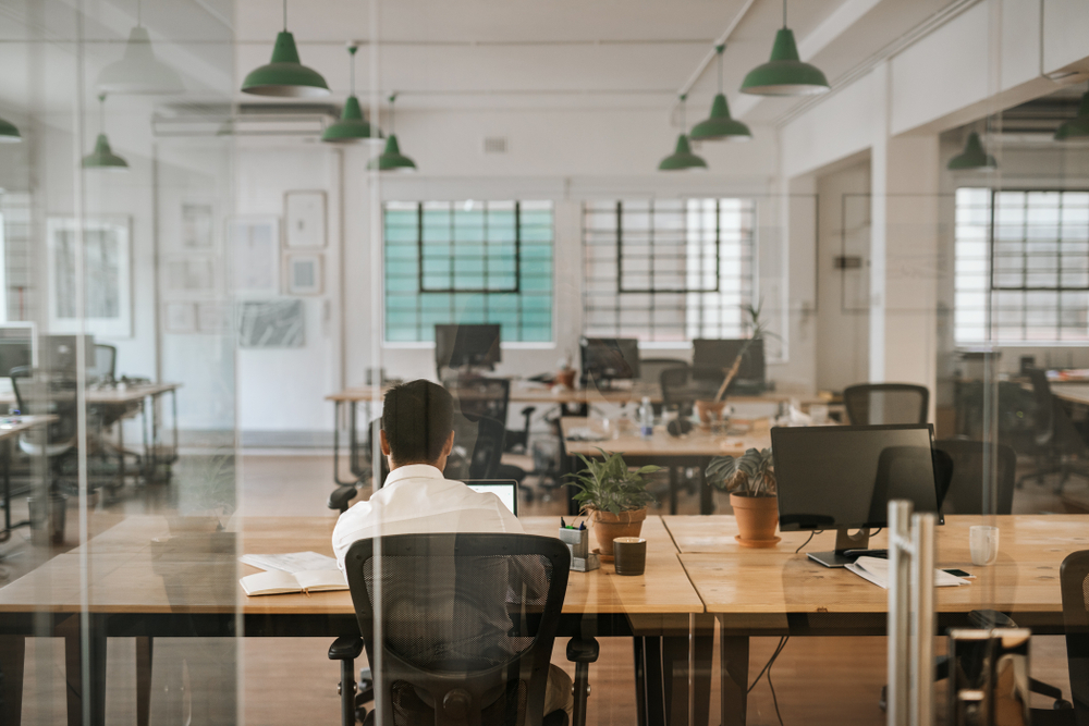 Rearview of a young businessman sitting alone at his desk in an office working on a laptop and going over paperwork