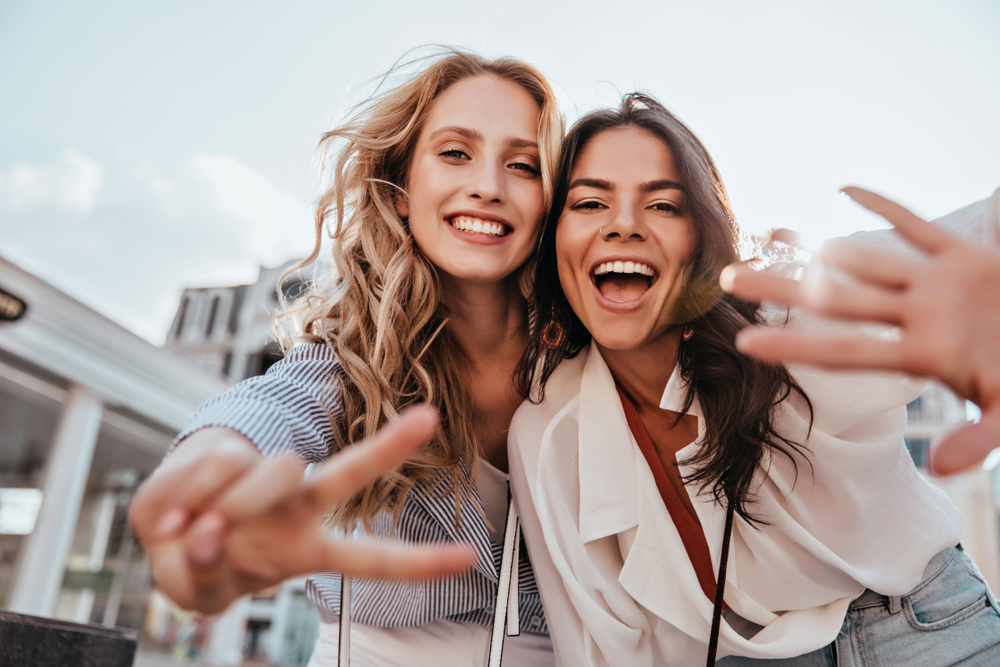 Lovable caucasian girls expressing positive emotions to camera. Outdoor photo of refined sisters posing on sky background.
