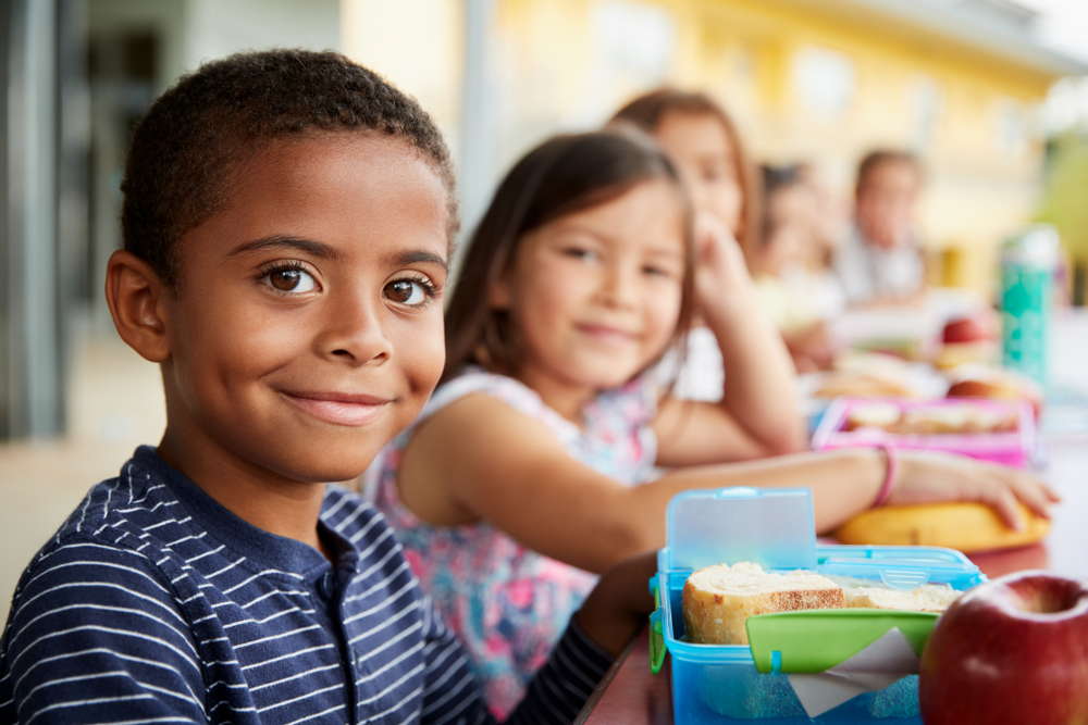 Young boy and girl at school lunch table smiling to camera