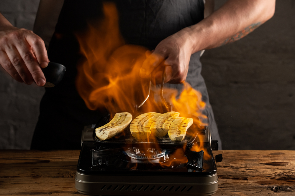 Cooking banana dessert on grill pan with burning flame. Chef service food concept.