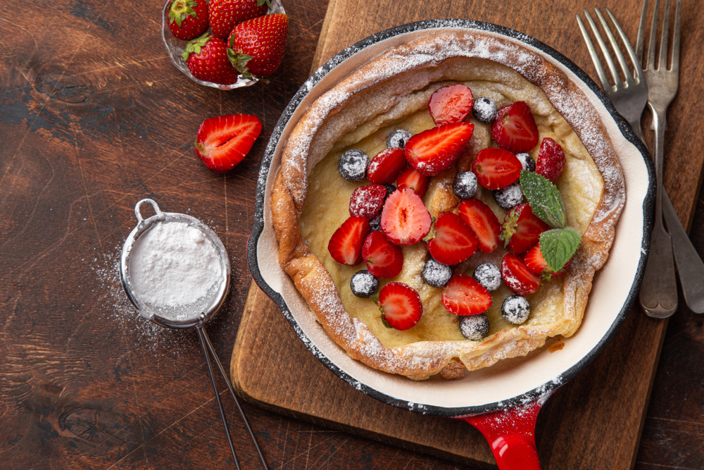 Dutch baby pancake with fresh berry in red pan for breakfast, top view, wooden background, copy space