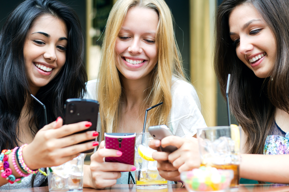 women sitting at table looking at their phones