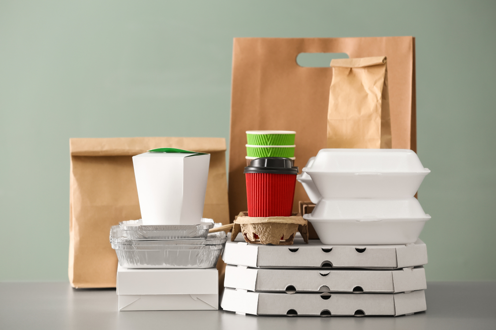 Different packages on table against color background. Food delivery service