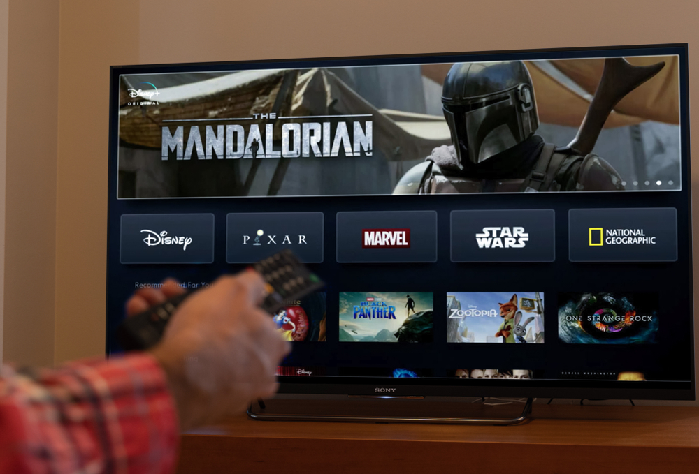 Barcelona, Spain. November 2019: Man holds a remote control With the new Disney plus screen on TV, showing The Mandalorian space western television series. .Illustrative editorial. Disney plus is an