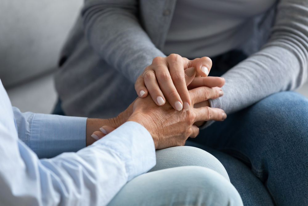 Young woman granddaughter daughter hold old female hand of mother grandma sit on sofa, two women generation help support concept, senior people parents grandparents care and comfort, close up view