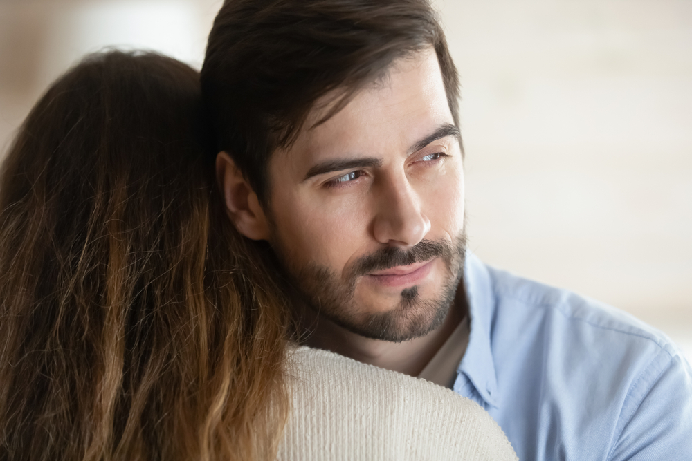 Thoughtful young man hug girlfriend or wife look in distance thinking pondering about relationship problems, millennial male liar or cheater make peace with beloved woman, fake forgiveness
