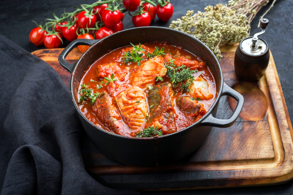 Traditional Brazilian fish stew moqueca baiana with fish filet in tomato sauce as closeup in a modern design cast-iron roasting dish