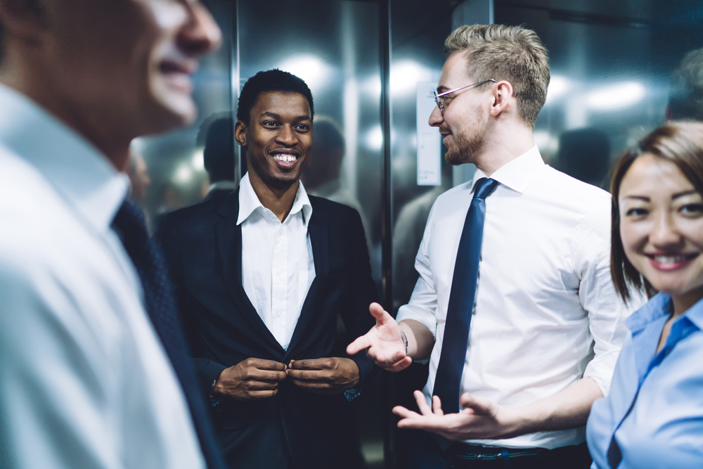 Group of multiracial cheerful successful coworkers smiling and talking while having fun and standing during elevator ride in modern company office
