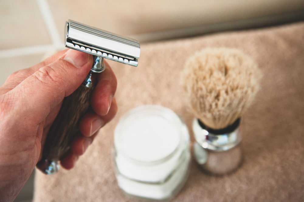 Close-up of safety razor 50s style and male cosmetic products and supplies used by men to shave. Safety razor, shaving brush and foam on beige towel background. Eco friendly tools for men shaving.