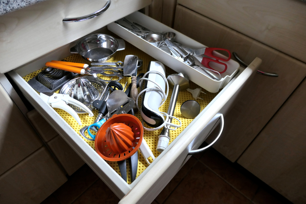 Many kitchen utensils in an open drawer. View of an open drawer with many household items in a kitchen.
