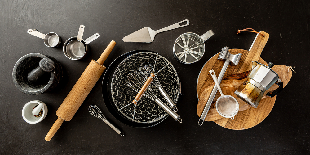 Kitchen utensils (cooking tools) on black chalkboard background - horizontal banner layout. Kitchenware collection captured from above (top view, flat lay).