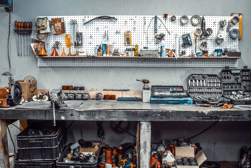 Moto workshop with hand tools. Workbench with sets of keys, screwdrivers, ploskobets, electrical tape, duct tape on the wall. Table with motorcycle parts, vise. Workspace for a joiner, auto mechanic
