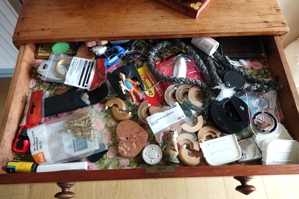 Dartmoor England. Looking inside a domestic drawer with a large jumble of small rarely used articles including, compass, picture hooks, Tin Tin and dog model, decorative rope, knife, film.