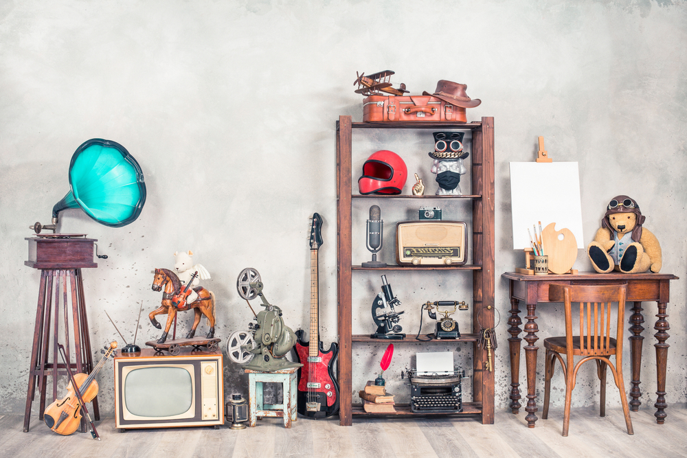 Antique media devices, writers tools, gramophone, film projector, old Teddy Bear toys and white canvas blank on easel, violin and guitar front concrete wall background. Vintage style filtered photo