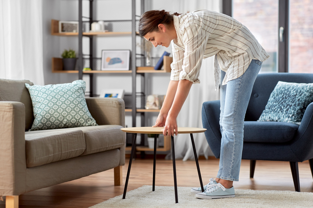 household, home improvement and interior concept - happy smiling young woman placing coffee table next to sofa