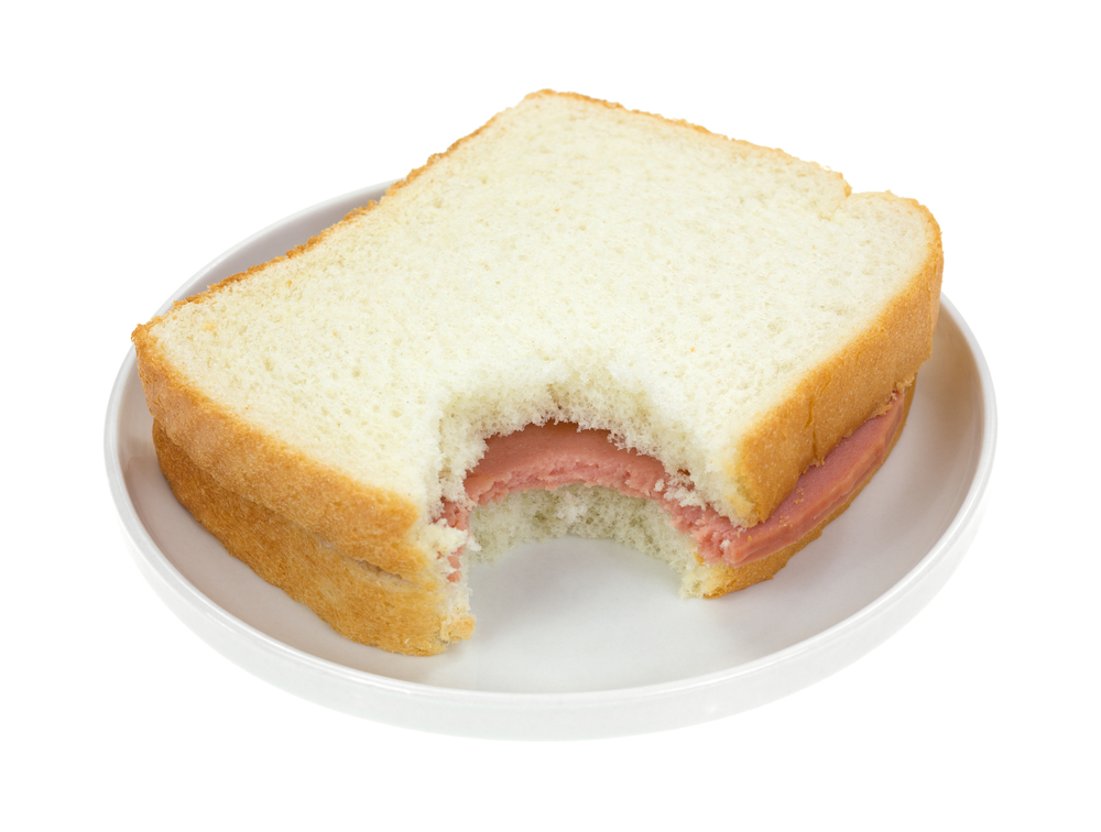 A bitten baloney sandwich with white bread on a small plate.