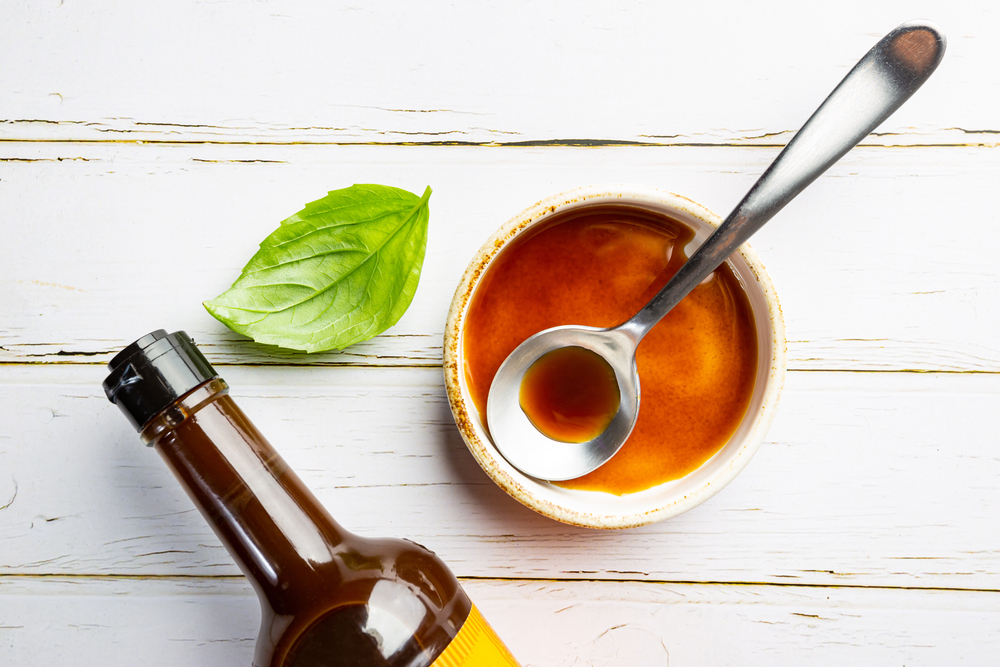 Worcestershire sauce in a bowl with spoon and bottle over white background, top view
