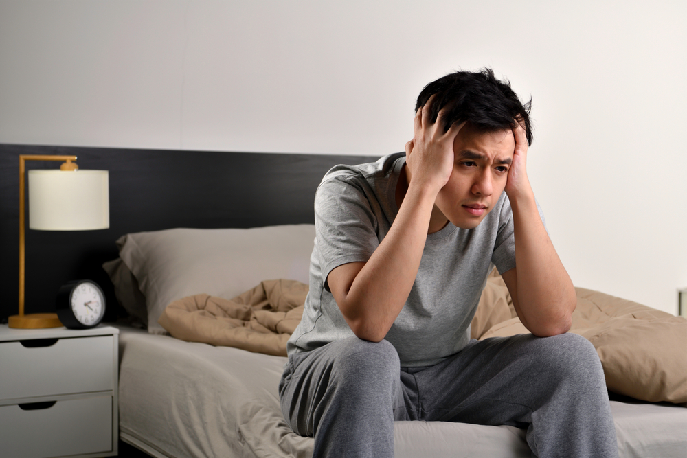 Depressed young Asian man sitting in bed cannot sleep from insomnia
