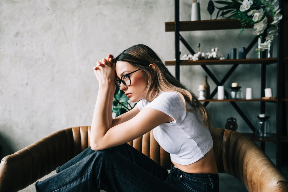 Young bored millennial woman sitting on a sofa alone at home. Fatigue or emotionally exhausted concept