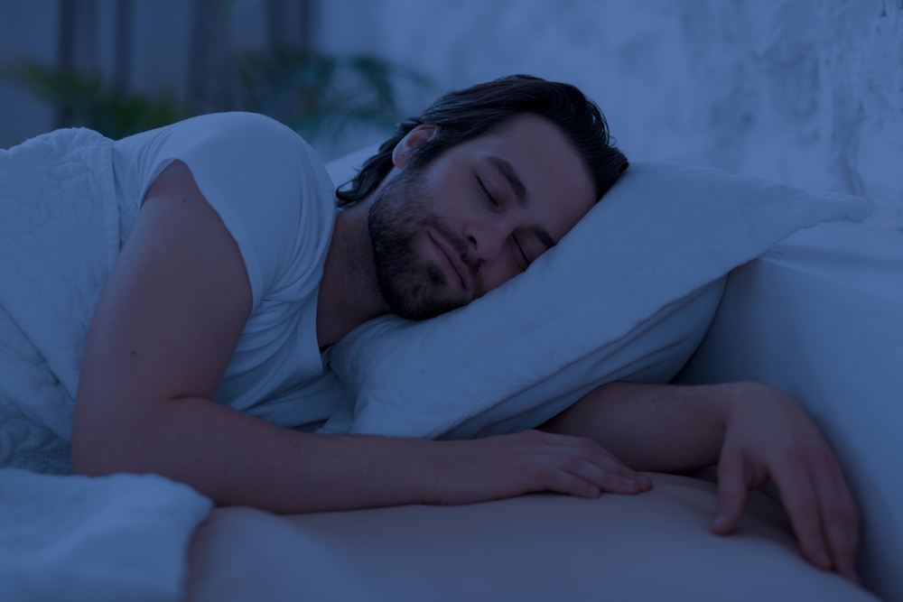 Peaceful handsome bearded young man sleeping in comfortable bed alone at home, enjoying his orthopedic mattress and pillow, side view, copy space. Good sleep concept