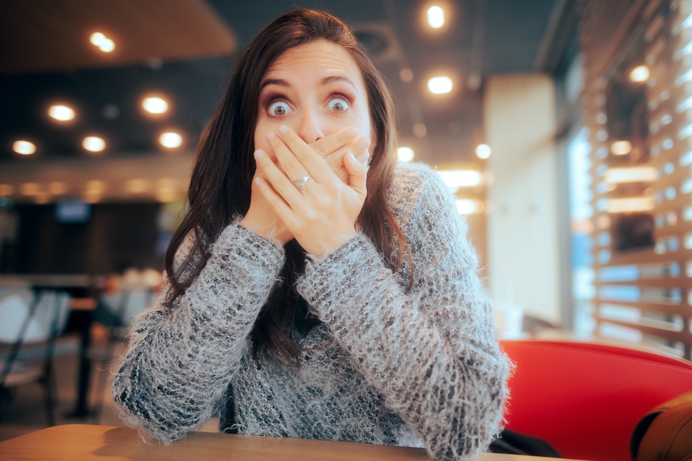 Shocked Woman Covering Her Mouth Sitting in a Restaurant. Lady feeling sick and nauseated from food poisoning
