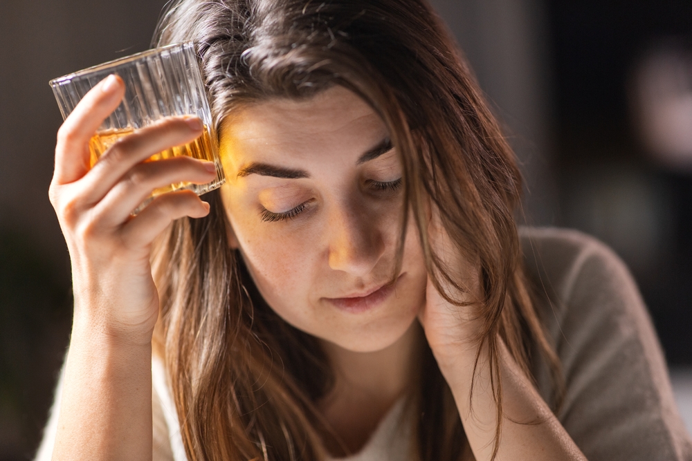 alcoholism, alcohol addiction and people concept - drunk woman or female alcoholic drinking whiskey at home