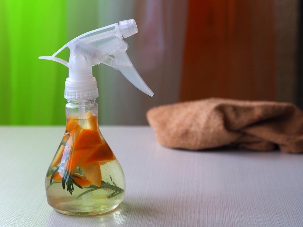 Flavored white vinegar with rosemary and orange zest in a clear spray bottle. Ecological detergent for cleaning the house. The concept of refusal to use harmful household chemicals.