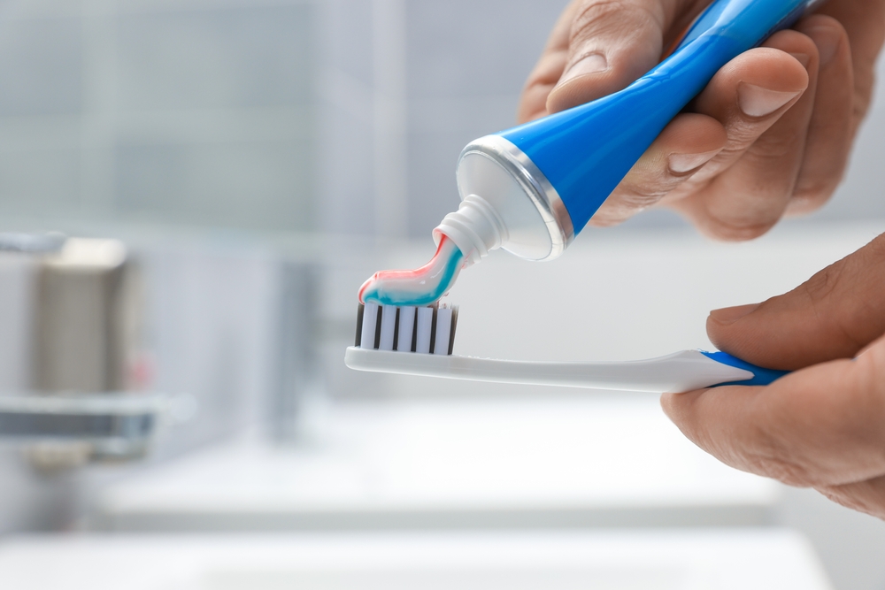 Man applying toothpaste on brush in bathroom, closeup. Space for text