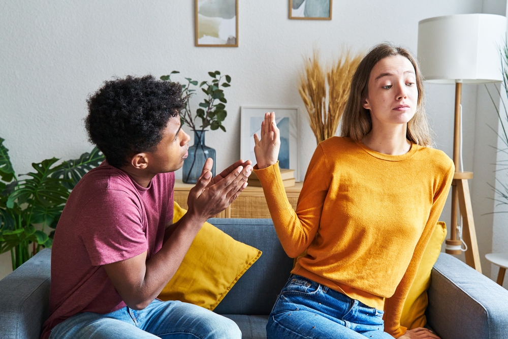 Black-skinned man begging for forgiveness and Caucasian woman turning him down in a house