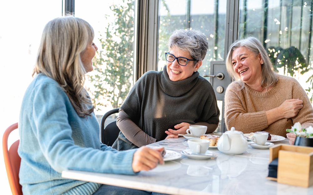 Group of elderly women have breakfast in a cafeteria, three retired female friends are celebrating an anniversary drinking tea and coffee and eating chocolate cakes
