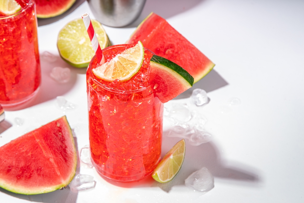 Watermelon lemonade with lime and sliced watermelon, on trendy high-colored white pink background