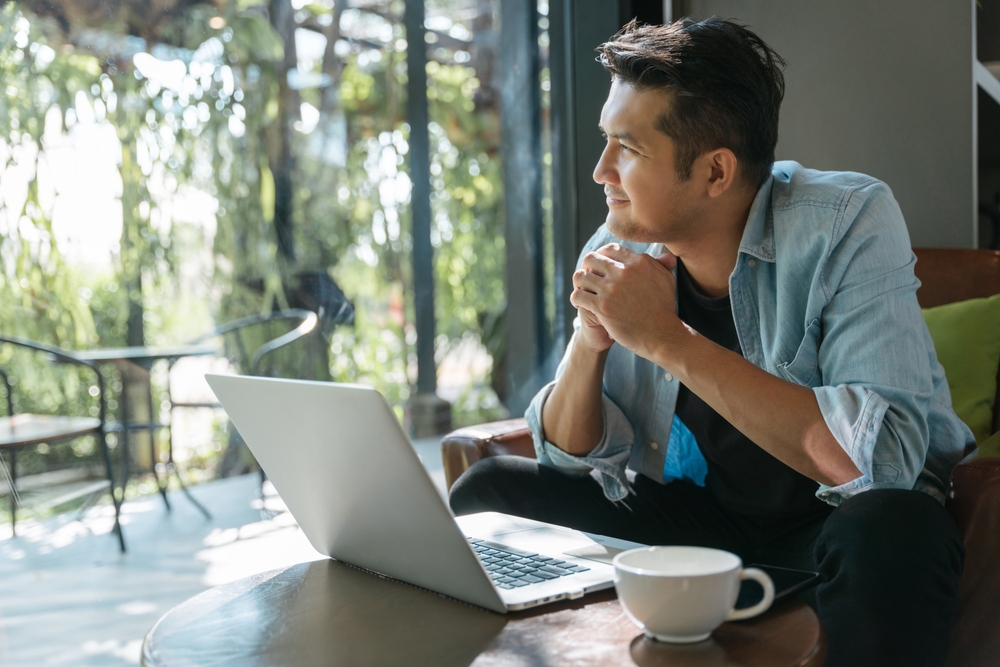 Asian handsome man sitting happily looking out of the window in a cafe. Concept freelance and financial freedom.