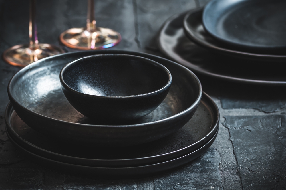 Black stoneware plates and bowls on a rustic black table
