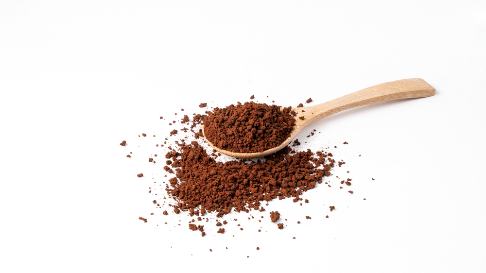 Roasted ground coffee in wooden spoon on white background.
