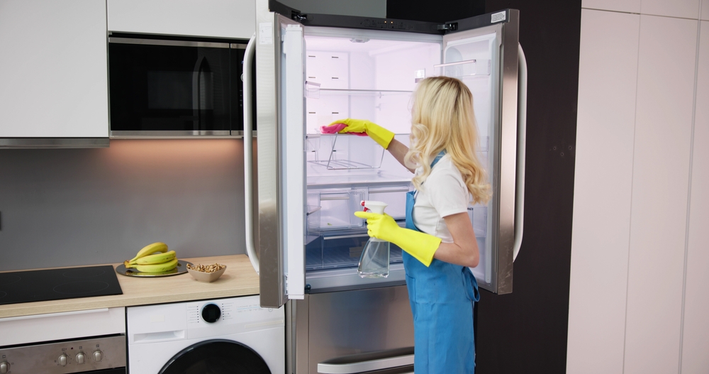 Young Smiling Professional Cleaning Service Woman Cleaning Refrigerator In Kitchen