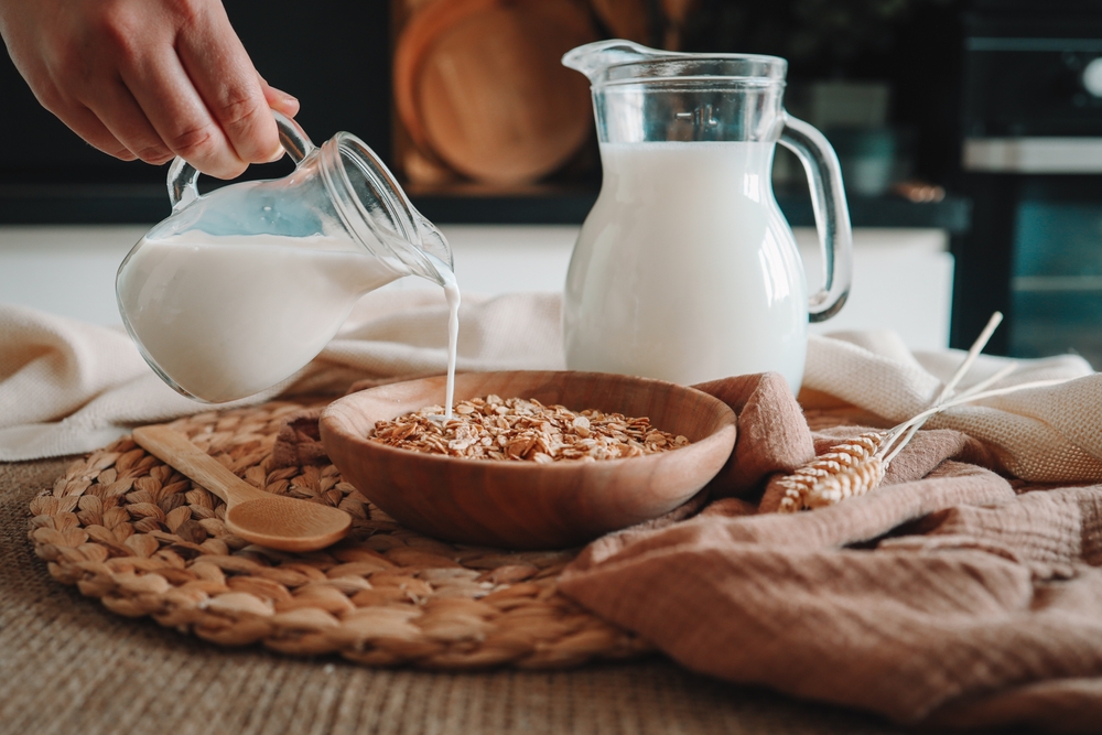 Milk jug pouring milk into the bowl with natural muesli made from mix of unprocessed whole grains.