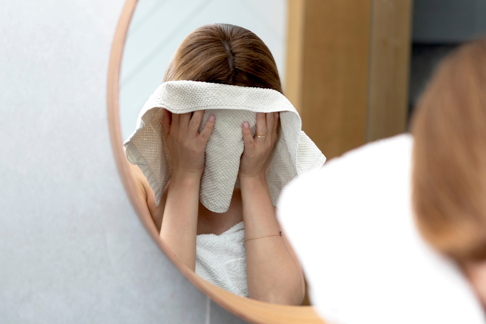Young woman wiping her face with towel in front of the mirror in the bathroom