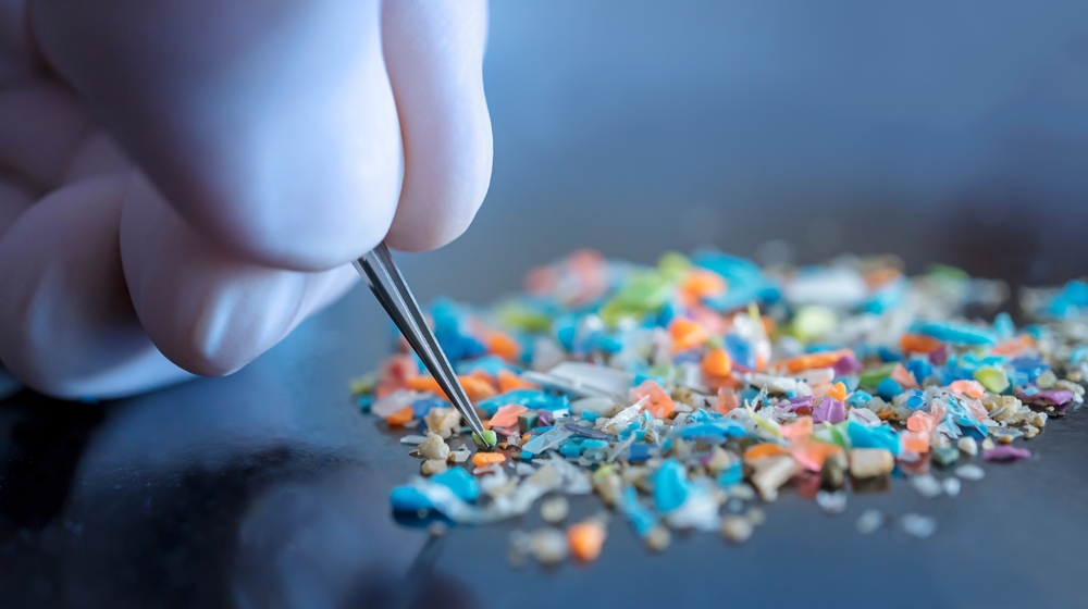 Macro shot of a person with medical gloves and tweezers inspecting a pile of micro plastics. Concept of water pollution and global warming. Macro shot of micro plastics. Cool blue filter applied.
