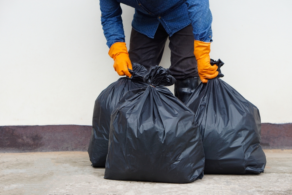 Closeup man holds black plastic bag that contains garbage inside. Concept , Waste management. Environment problems. Daily chores. Throw away rubbish . Sorting type of garbage.