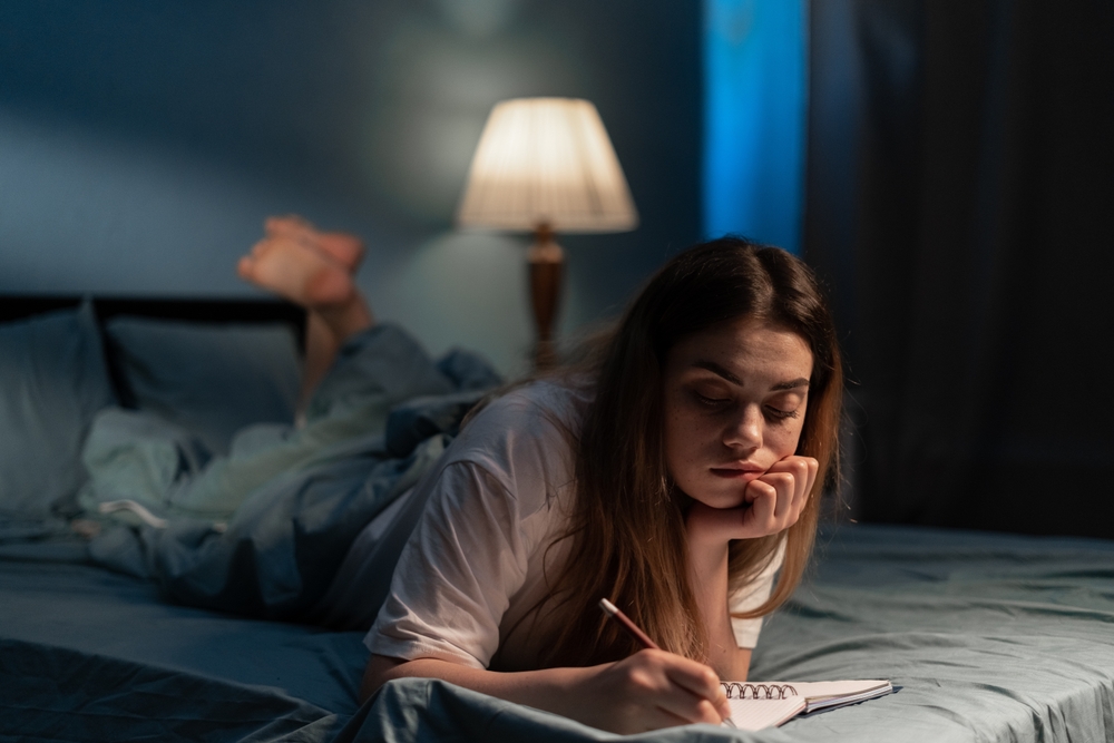 Beautiful woman writing diary in her bed at night. Diary planning. Copy space